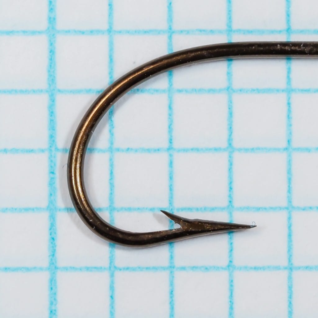 Mustad 3371 — point detail showing superior-point geometry with concave inner face — size 1/0 — bronzed finish on 1/10-inch grid