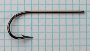 Mustad 3310 size 18 full side profile showing a blind marked shank, rounded bend, barbed point, and bronzed finish on a measurement grid.