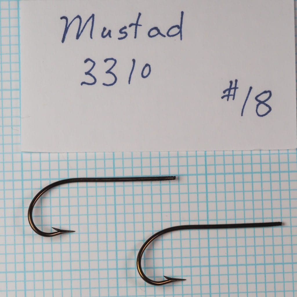 Two Mustad 3310 hooks identified as size 23 beside a handwritten specimen card on a measurement grid.