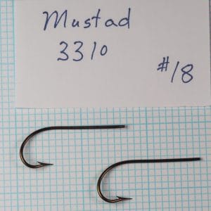 Two Mustad 3310 hooks identified as size 23 beside a handwritten specimen card on a measurement grid.
