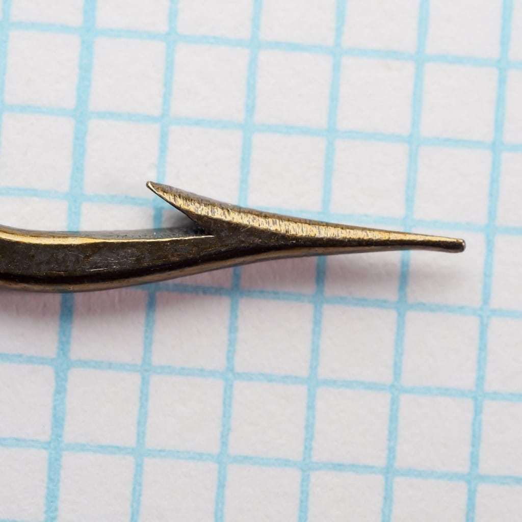 Mustad 3401 A hook point — close-up showing superior point geometry and sharp tapered tip — size 5/0 — bronzed finish on measurement grid