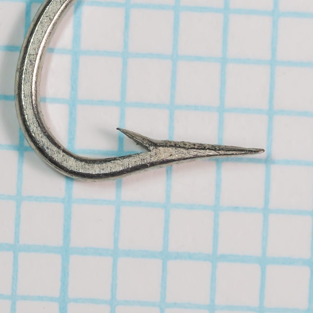 Mustad 3404 hook point close-up — showing Superior point geometry with near-straight inner taper, tinned finish, size 1/0, on measurement grid