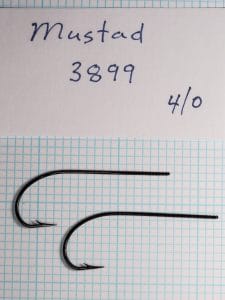 Two Mustad 3899 Sproat hooks size 4/0 on metric grid showing scale comparison.