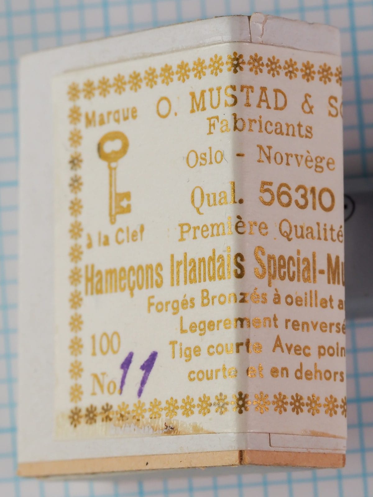 Mustad 56310 — cylindrical cardboard box and cream-colored kraft paper wrap-around label with gold metallic letterpress printing showing Key Brand logo and French text 'Hameçons Irlandais Special-Montés' — size No. 11 — mid-1950s to 1960s Oslo-Norvège packaging