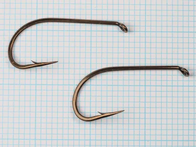 Mustad 9617 — complete hook profile — two specimens, size 6/0 — showing eye loop, shank, bend, and point geometry — bronzed finish — against 1/10-inch measurement grid