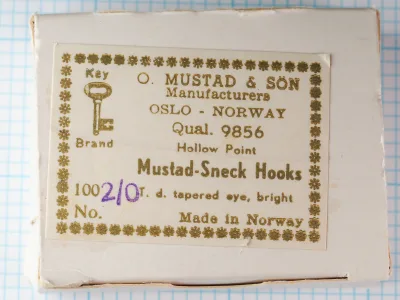 Mustad box lid with a gold-printed Key Brand label reading Qual. 9856, Hollow Point, Mustad-Sneck Hooks, with size 2/0 written in purple.