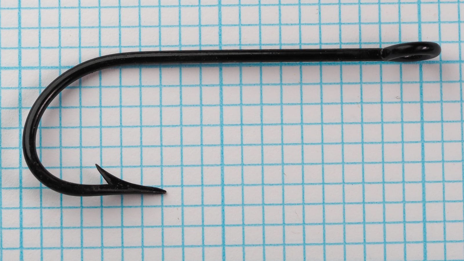Pflueger 3221-J Hook — side profile showing full bend geometry, ringed eye, and kirbed offset — japanned black finish — on measurement grid