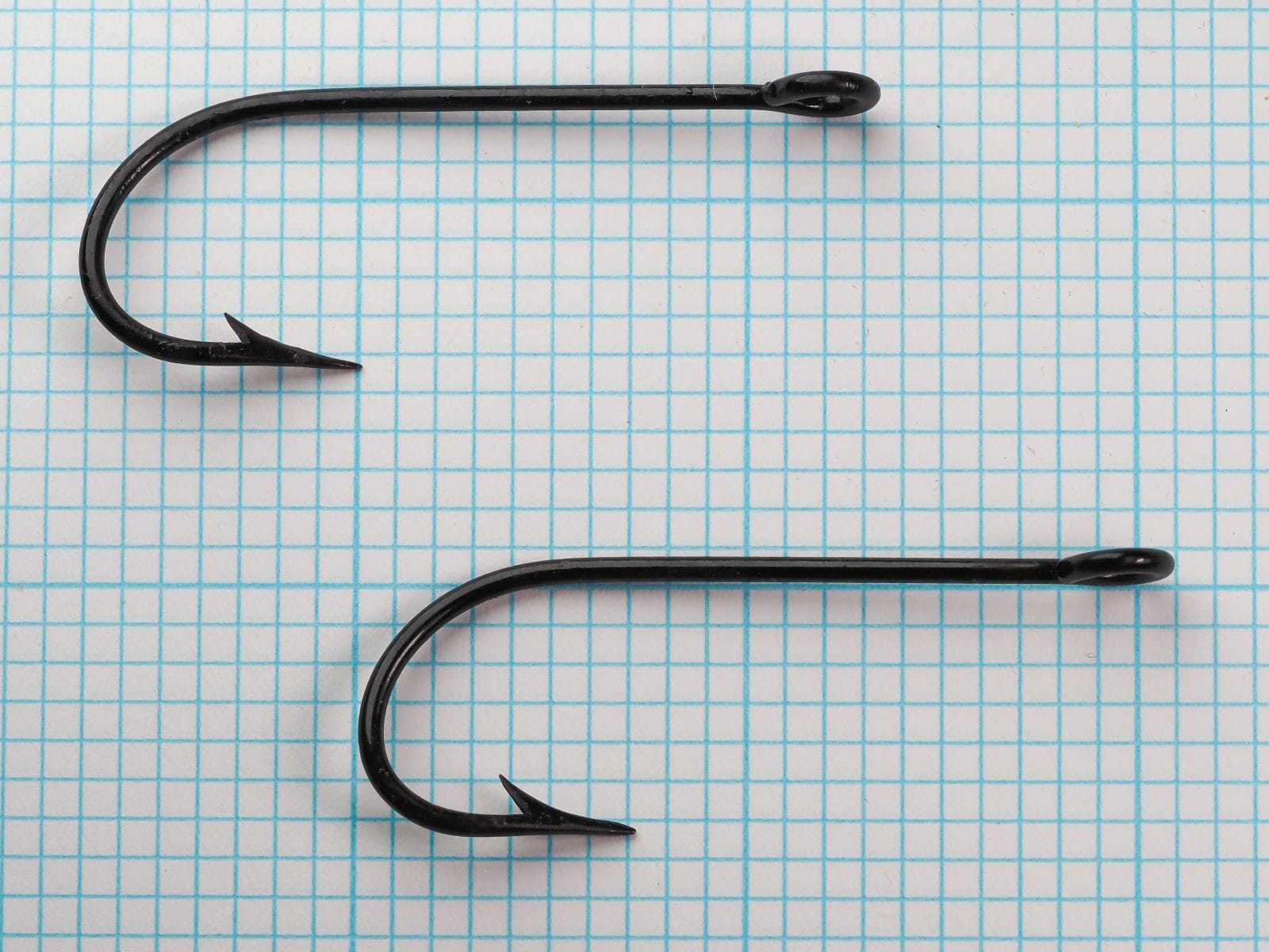 Pflueger 3221-J Hooks — two hooks side by side showing consistency of bend geometry and finish — size 6/0 japanned — on measurement grid