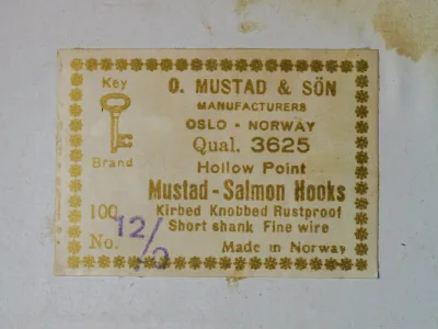 Mustad 3625 retail box — cream-colored vintage packaging with gold-printed label, hand-stamped size notation 12/0 in purple ink