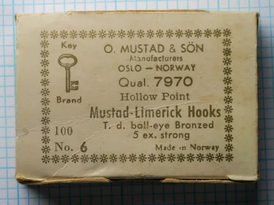 Mustad 7970 sales card — cream kraft paper with ornate border and eight-line label showing model code, point type, bend pattern, eye type, wire strength, and finish — size No. 6, 100-hook box