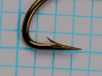 Mustad 7970 hook point detail — showing hollow point geometry with concave inner face, barb placement, and acute point angle — size No. 6 on measurement grid