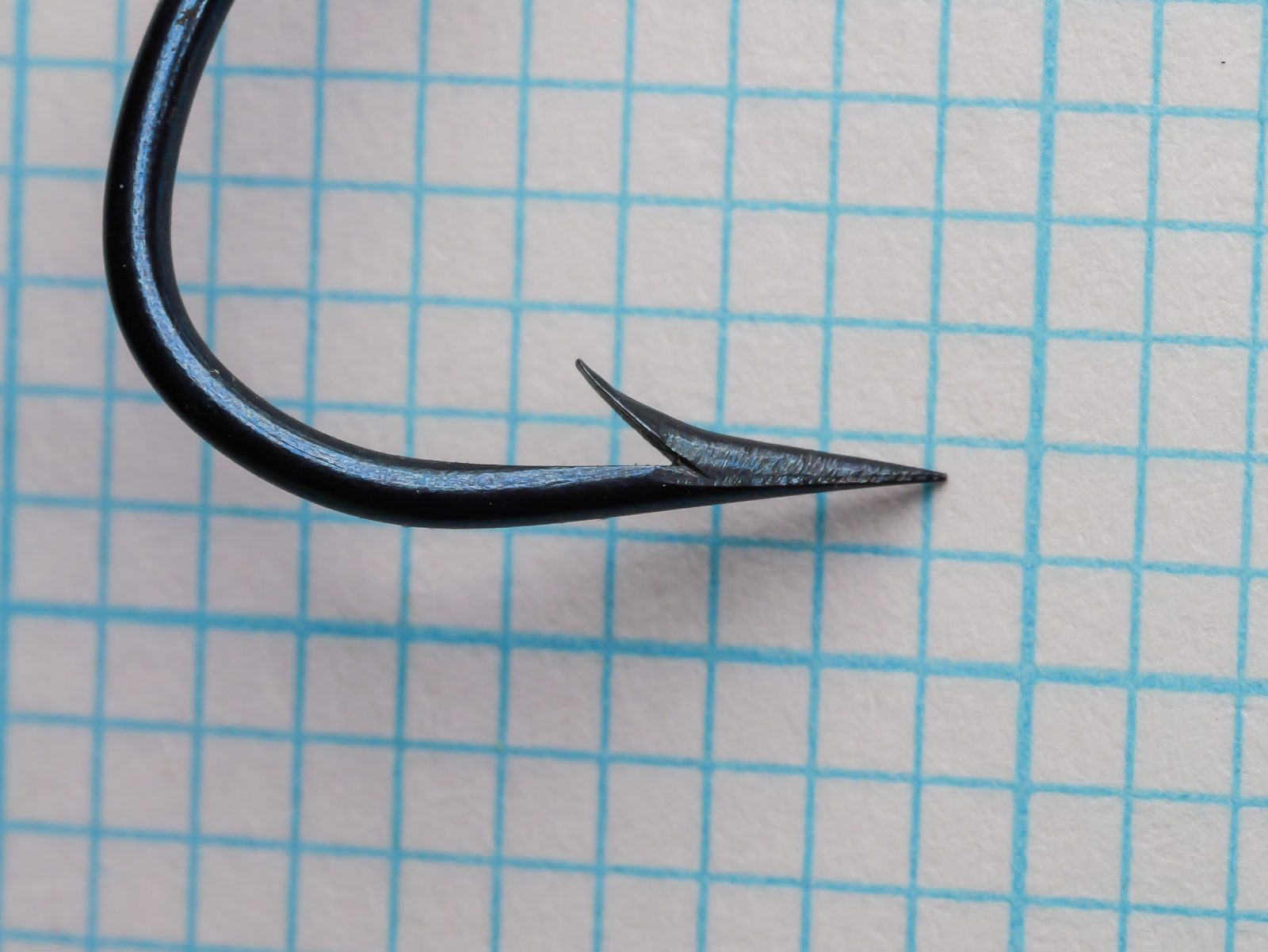 Milward 2599 Hook point detail — close-up of hook point and barb showing hollow point geometry and blued finish — size 4/0 — photographed at angle on measurement grid