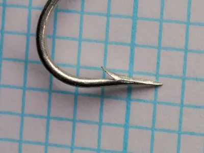 Close-up profile view of single tinned Mustad 3576 L hook showing Carlisle bend and point geometry