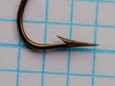 Mustad 3777 Central Draught — profile view of hook showing hollow point geometry and pronounced kink in shank — size 3/0 — bronzed finish on measurement grid