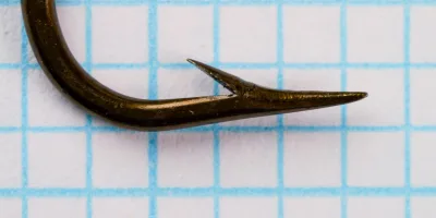 Mustad Quality 3828 — hook point detail showing hollow point geometry — size 3/0 — side profile on measurement grid