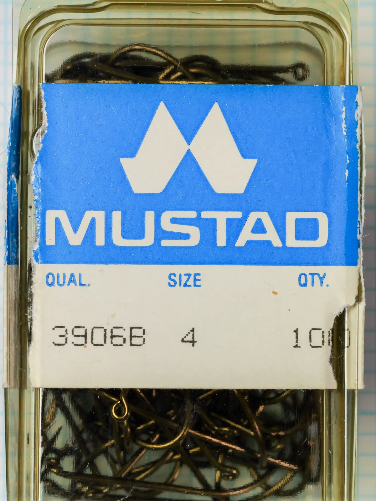 Mustad 3906B size 4 plastic box with a blue and white MUSTAD label band and loose hooks inside.