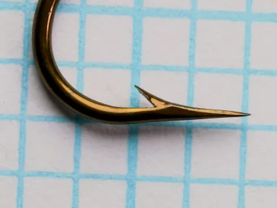 Close-up of the point and barb of a Mustad 3906B size 4 hook on blue grid paper.