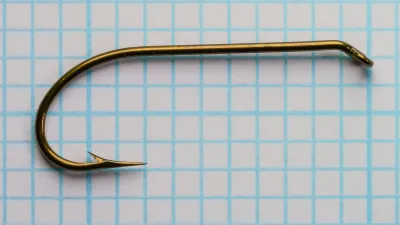 Side view of a bronzed Mustad 3906B size 4 hook on blue grid paper.