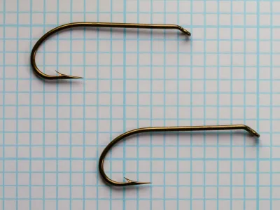 Two bronzed Mustad 3906B size 4 hooks side by side on blue grid paper.