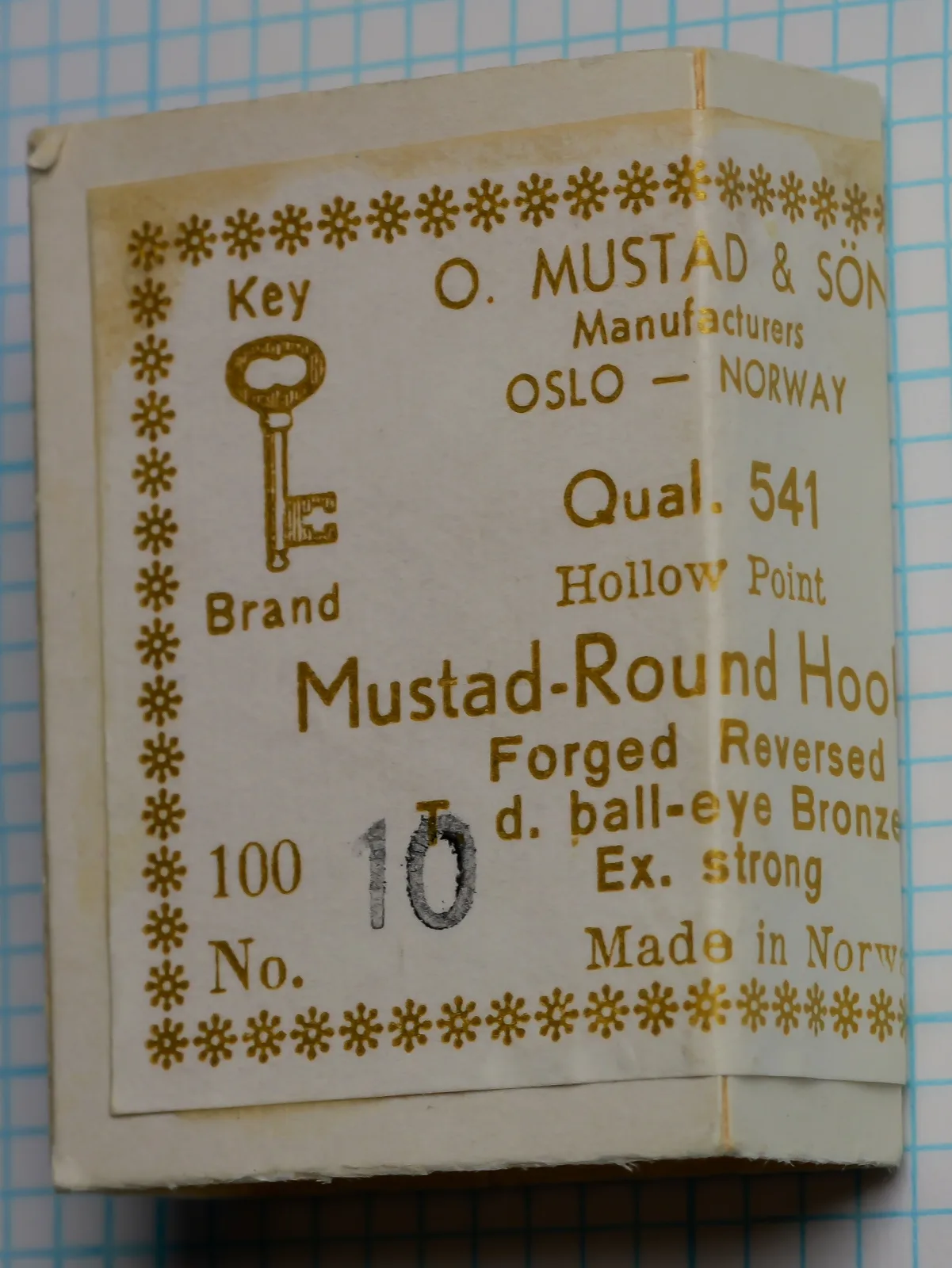 Upright front of a Mustad Qual. 541 box with a gold Key Brand label, a pencil 10 at lower left, and a yellow-brown stain along the upper label margin