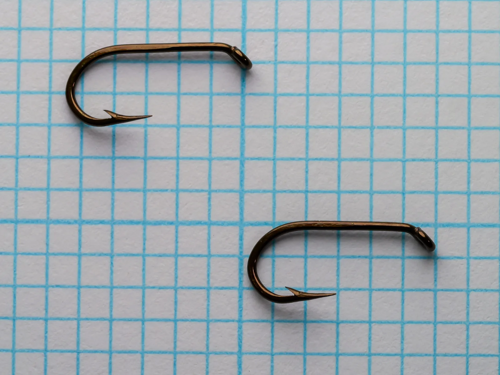 Two Mustad 541 hooks lying flat side by side on a blue grid