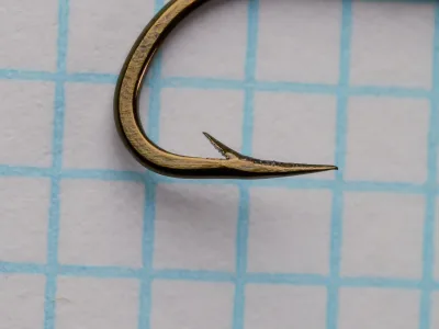 Mustad 92621 hook detail — close-up of hollow point and barb geometry showing concave inner face and reversed offset — on measurement grid