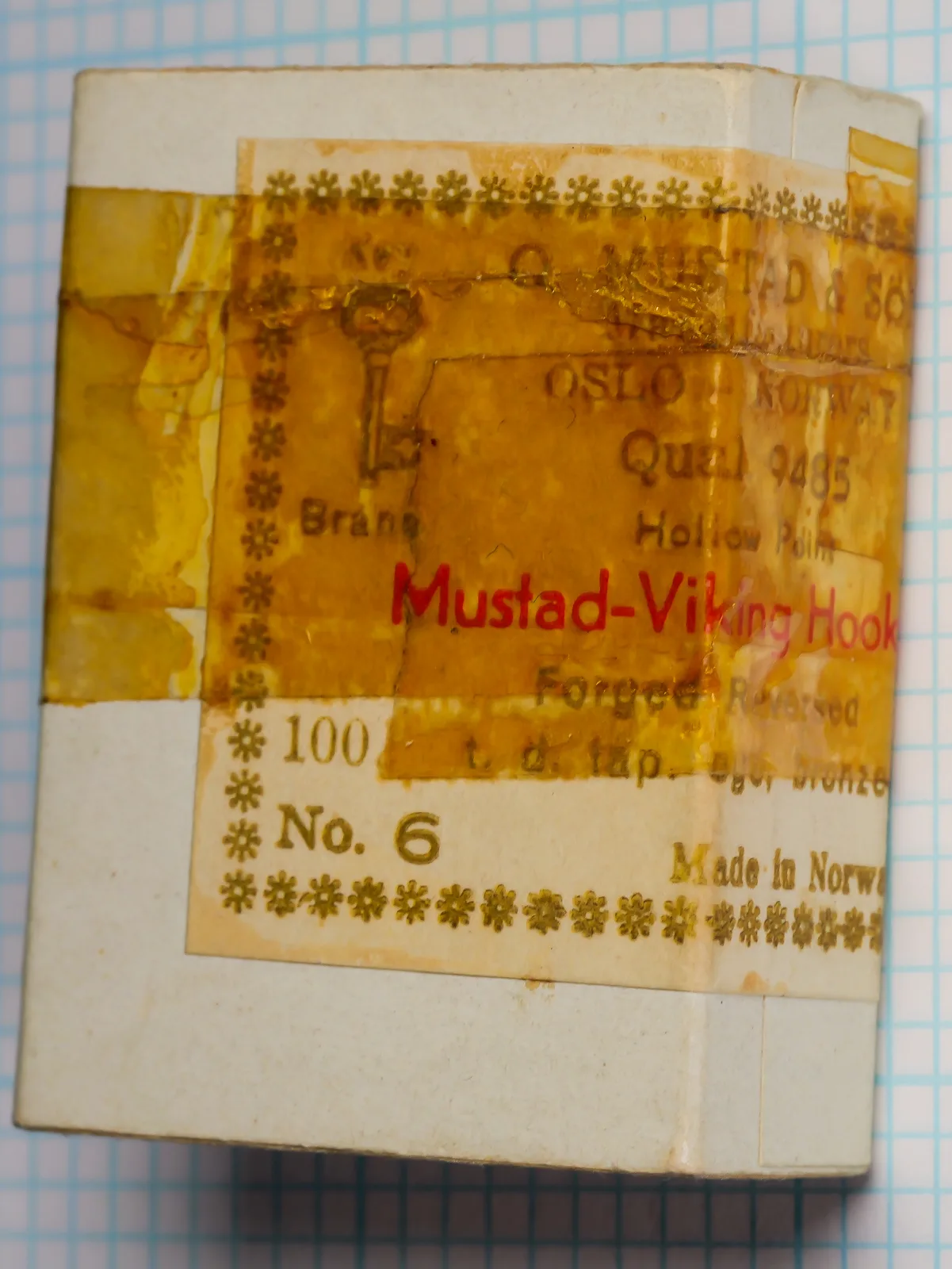 Mustad 9485 size 6 box upright, with a gold and red label under amber tape.