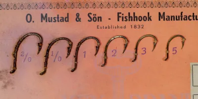 Mustad 92154 Beak Hooks — six size samples mounted on vintage sales card — sizes 2/0 to 5 — bronzed finish visible