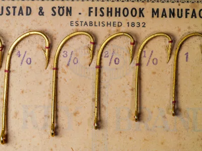 Mustad 92624 Beak Hooks — close-up of five gold-plated hooks on original sales card showing reversed offset bend and ringed eye detail with hand-written size markings in purple pencil