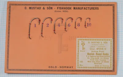 Mustad 9555 B salesman's sample card — orange cardstock with six nickelplated hooks mounted in graduated sizes (No. 1–10) with red glass bead size markers — full card view showing decorative geometric border and Key Brand logo