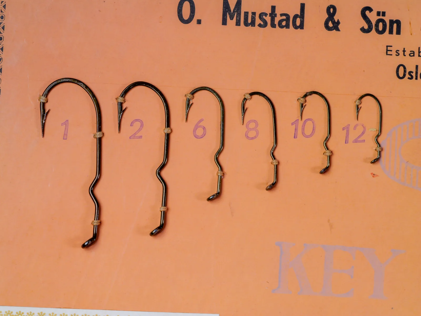Mustad 9661 — sales card showing six specimen hooks in sizes 1, 2, 6, 8, 10, 12 — kinked shank and extended 4X length visible — bronzed finish