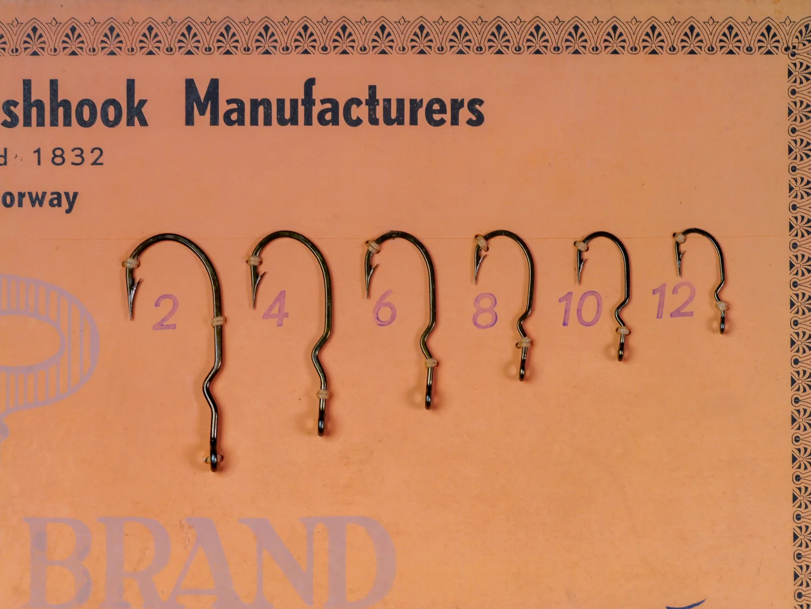 Mustad 9664 Sales Card — Six hooks displayed on orange card stock showing size range 2, 4, 6, 8, 10, 12 — demonstrating kinked shank geometry across sizes