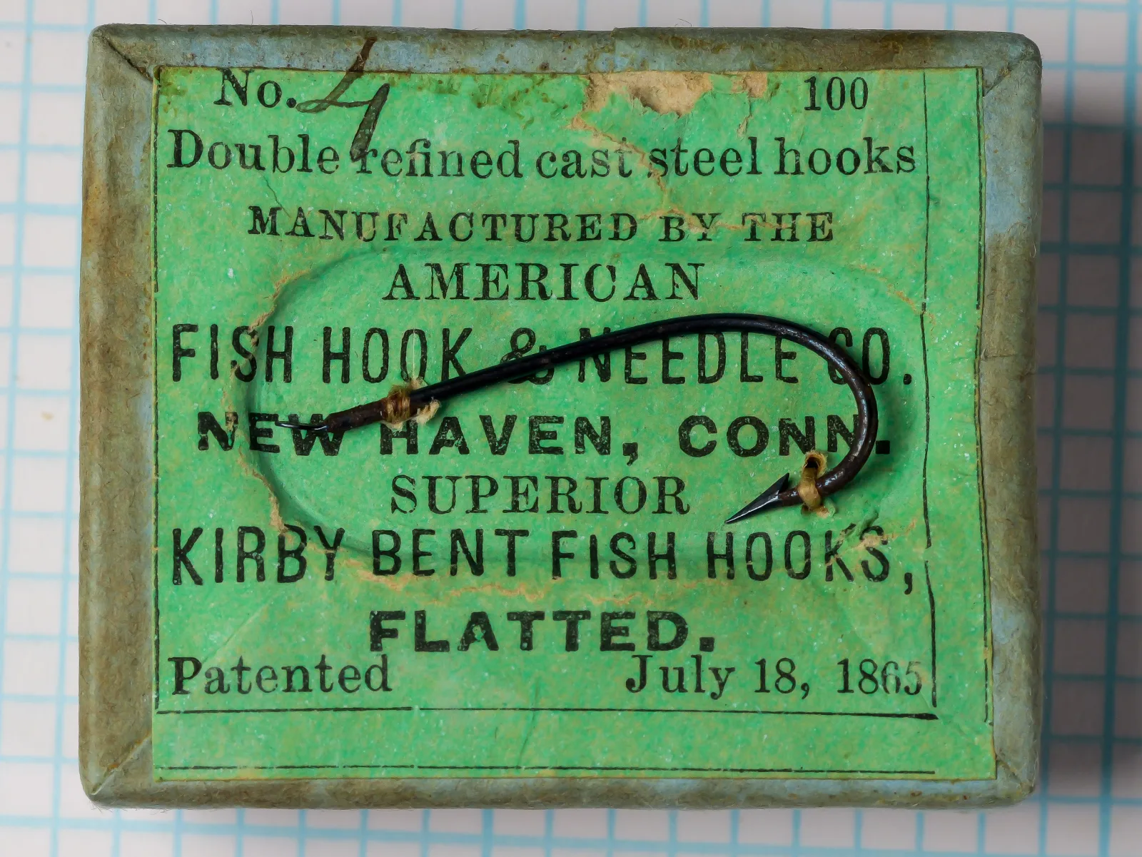 American Fish Hook and Needle Company box and label — front face showing green japanned tin box with black letterpress label identifying Superior Kirby Bent Fish Hooks Size 4, patented July 18, 1865 — New Haven, Connecticut manufacture — 100-hook box