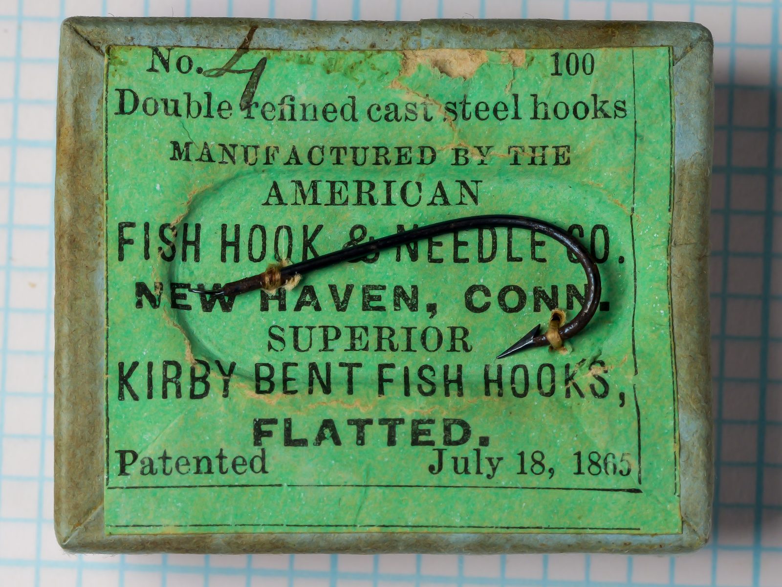 American Fish Hook and Needle Company box and label — front face showing green japanned tin box with black letterpress label identifying Superior Kirby Bent Fish Hooks Size 4, patented July 18, 1865 — New Haven, Connecticut manufacture — 100-hook box
