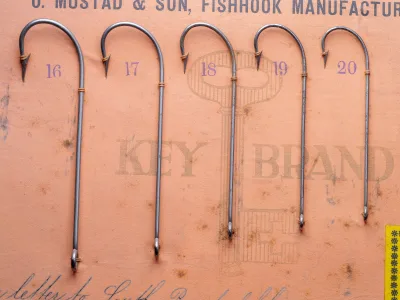 Mustad 3304 Cincinnati Bass Hooks — five specimens sizes 16–20 mounted on measurement grid — bright steel finish with ringed eyes