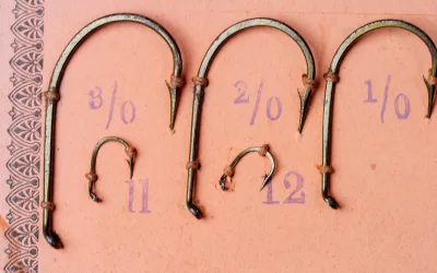 Mustad 7958 A salesman sample card hooks — multiple sizes pinned on card including size 16 specimen — demonstrates size range 3/0 to 12, round-bend profile with tapered eye