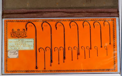Wm. Bartleet M58 Archer Carlisle Ringed sales card display — full card showing mounted hook examples in sizes 1/0 through 7/0 on orange card stock with decorative letterpress border and label