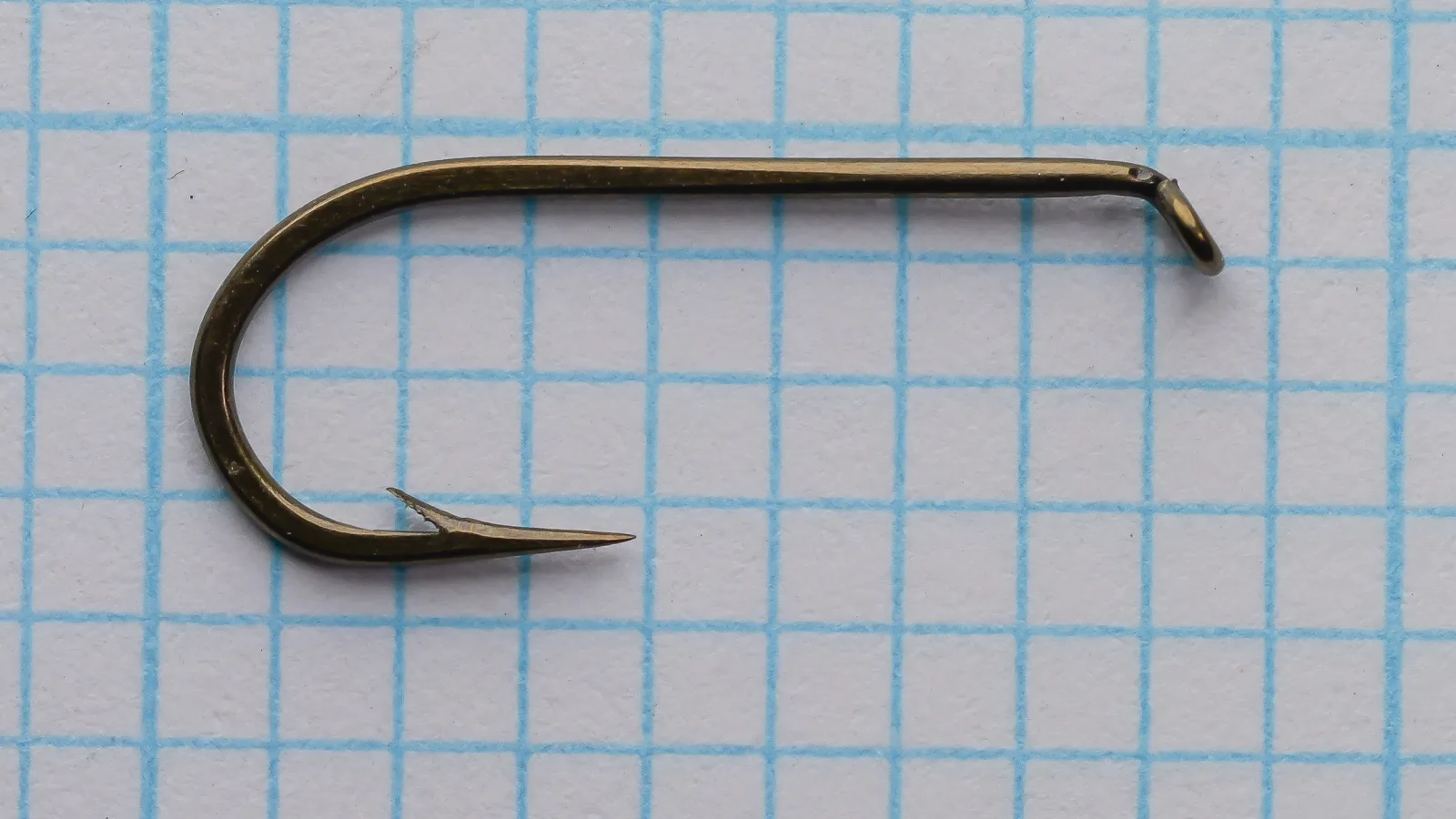 Mustad 7948 A bronzed round Kendal bend hook, side view against grid