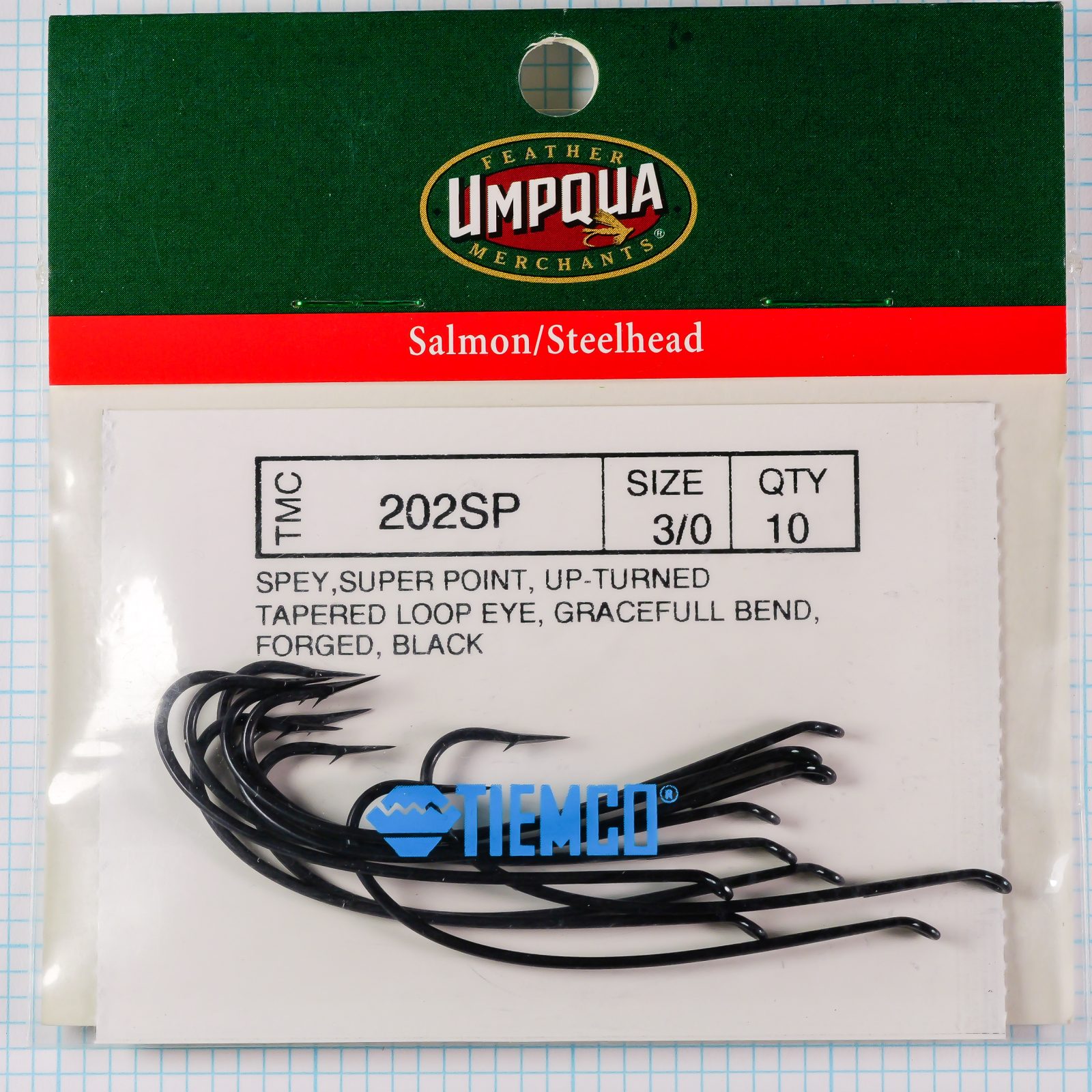 TMC 202SP complete retail package — Feather Merchants Impqua brand header — japanned hooks visible in plastic case on measurement grid — size 3/0