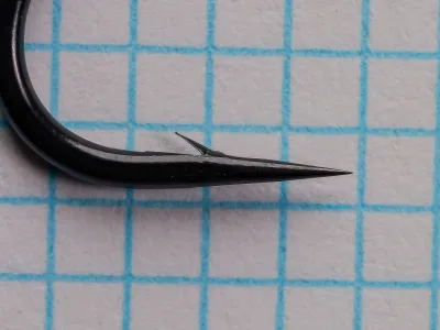 Tiemco TMC 7999 Hook Point — side profile showing hollow point geometry — size 1/0 — barb detail on 1/10-inch grid