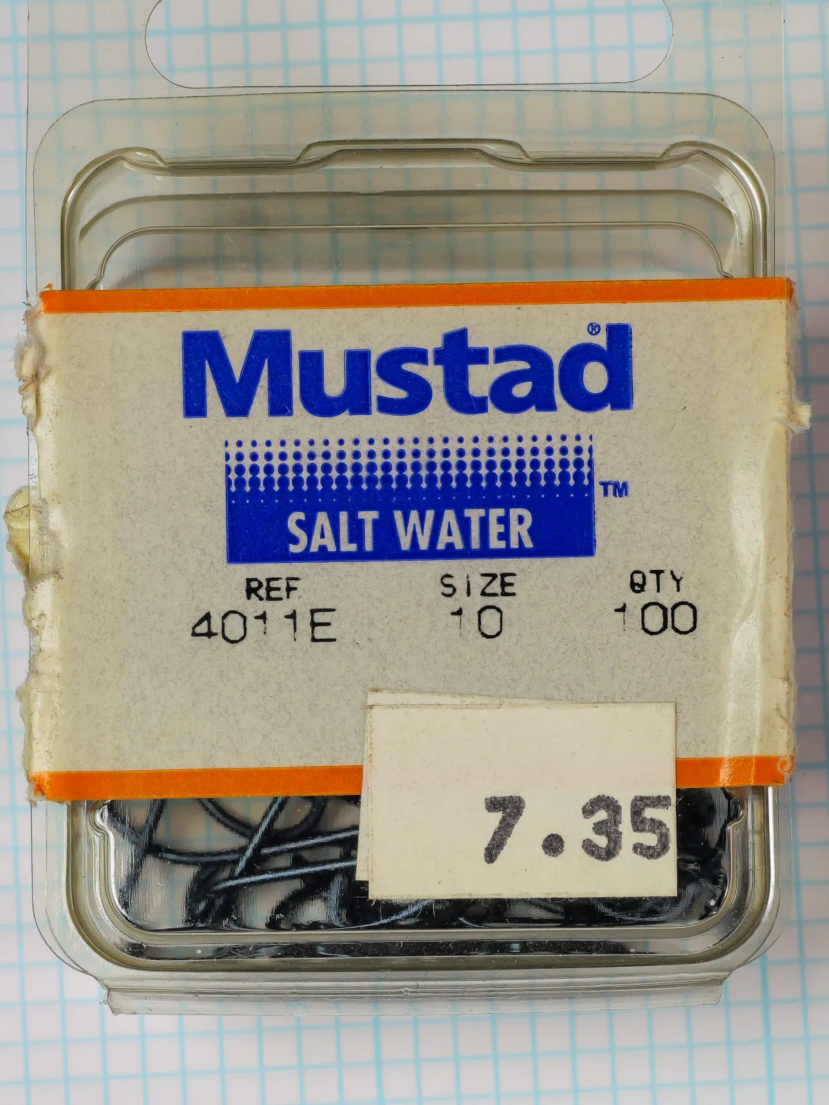 Mustad 4011-E Size 10 — original plastic clamshell packaging with cardboard insert, orange tape bands, and offset-printed label showing model code and size — vintage saltwater hook