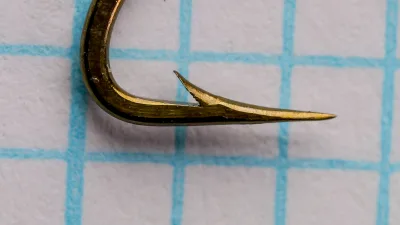 Mustad 9575 Limerick — hook point detail showing hollow point geometry and barb — size 10 — bronzed finish, photographed on measurement grid