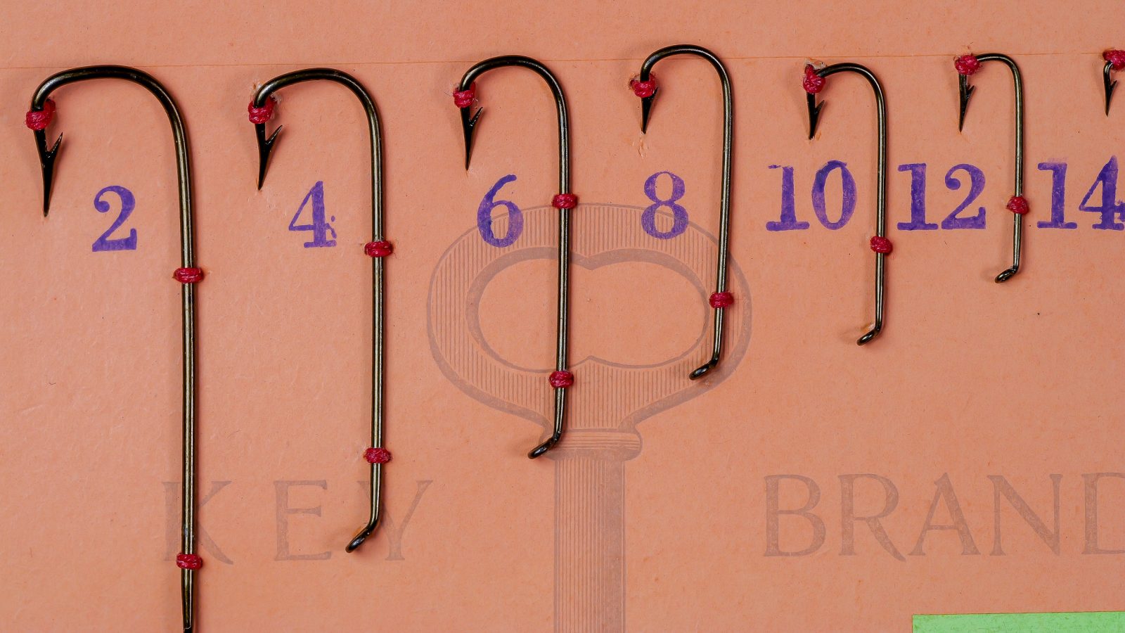Mustad 3349 Sneck Hook — six sizes displayed on lime-green card with measurement grid — sizes 2, 4, 6, 8, 10, 12, 14 — bronzed finish with red thread securing