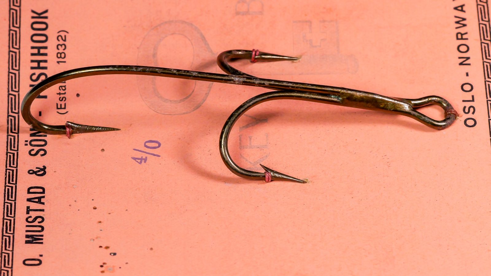 Mustad 7799 Double Kirby Hooks — side-by-side profiles showing two specimens size 4/0 — forged bend and hollow point geometry — bronzed finish on measurement grid