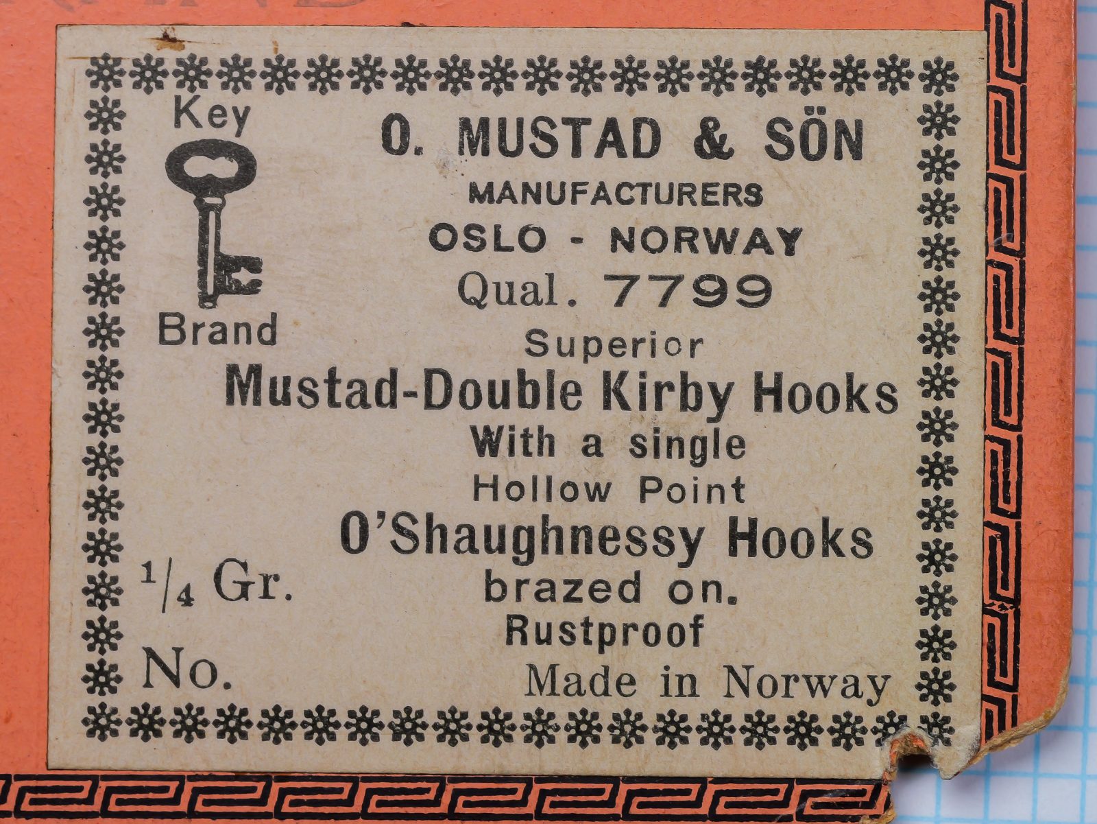 Mustad 7799 packaging label — cream-colored insert on orange sales card — letterpress printing with Art Deco border — size 4/0 designation