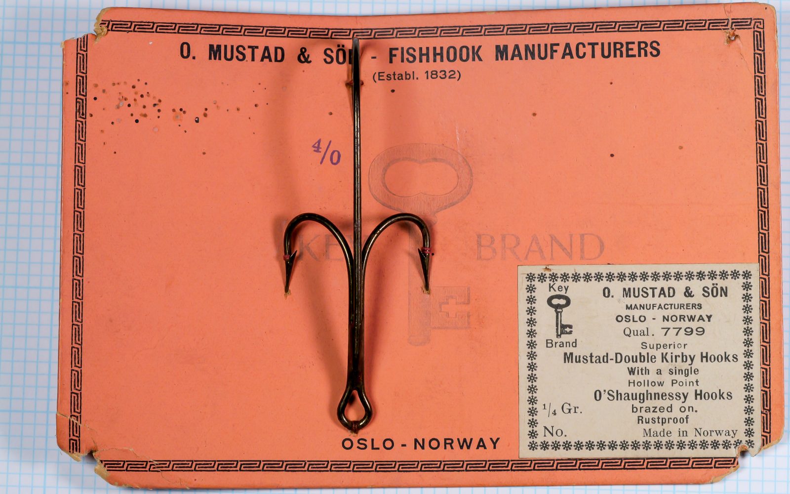 Mustad 7799 complete sales card — size 4/0 — orange card with pasted cream label insert — two bronzed hooks visible — Art Deco border design