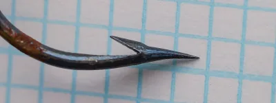 Allcock 3736M hook — profile view showing bend, long shank, kirbed offset, and pointed tip — size 4/0 — blued finish on measurement grid