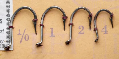 Mustad-Round Hooks 77830 — close-up of four specimens showing hook profile, eye detail, and point geometry — size 1/0, 1, 2, 4 — nickelplated finish