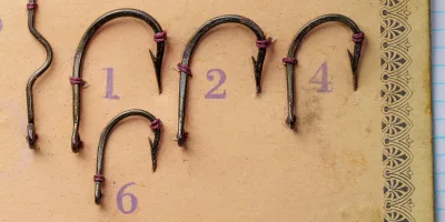 Close-up detail of Mustad 77880 hooks showing reversed offset geometry, straight tapered ring eye, and bronze finish on numbered mounting positions on tan card