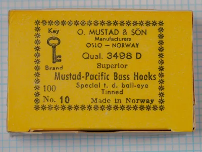 Mustad-Pacific 3498 D manufacturer box lid—yellow card stock with ornamental key-border design, printed text stating Oslo–Norway origin, model 3498 D, 100 No. 10, tinned finish, special ball-eye specification
